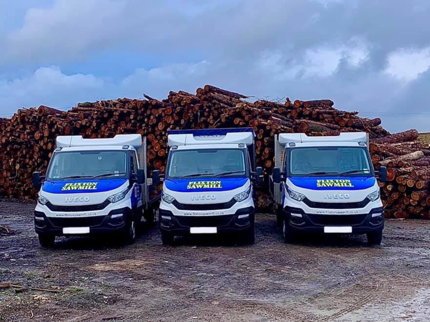 Three vans parked in front of a pile of logs